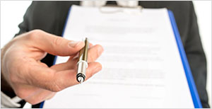 Hand offering pen to sign document on clipboard